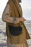 Minimal Toscana cross body bag in black with curved design and adjustable strap worn with beige outfit