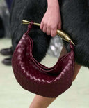 Maroon woven handbag with gold-tone sardine hardware and leather design held by hand