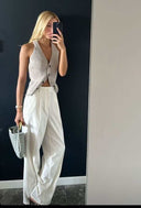 Woman holding Orla woven handbag with gold-tone hardware, wearing beige top and white pants
