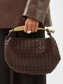 Brown woven handbag with gold-tone handle held by a person wearing a brown leather jacket