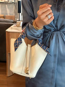 Elegant white vegan leather bucket bag with gold hardware and patterned scarf detail held by a person in a blue satin dress