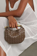 Brown Orla woven handbag with gold-tone hardware held by person in white dress