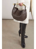 Brown woven handbag with gold-tone hardware held by person wearing white coat and black boots