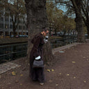 woman walking outdoors holding black Aveline handbag with adjustable strap and wearing long dark coat