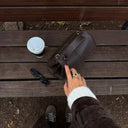 Aveline vegan leather handbag in ebony with adjustable strap on wooden bench beside coffee and sunglasses