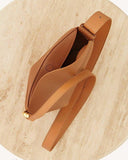 tan Toscana cross body bag with smooth texture and curved design on stone surface