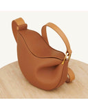 brown Toscana cross body bag with curved shape and smooth texture on beige surface