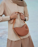minimal Toscana cross body bag in tan leather with curved design and gold hardware worn over beige outfit