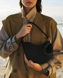 Toscana black cross body bag with curved design and smooth texture worn with beige coat