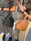 Two women holding stylish Piana Bucket bags in black and brown vegan leather with gold hardware accents
