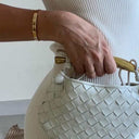 White Orla woven leather handbag with gold-tone hardware held by woman in white outfit