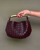 Orla woven leather handbag with gold-tone stainless steel handle held by hand against plain background