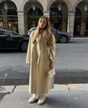 Woman wearing beige long coat holding Loriana Crossbody Handbag in urban street setting