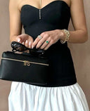 Black vegan leather crossbody handbag with adjustable strap and silver logo emblem, styled with a black and white outfit